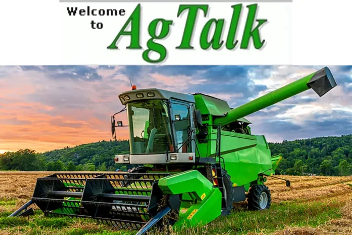 AgTalk image showing a green combine harvester in a harvested field at sunset with hills and trees in the background.