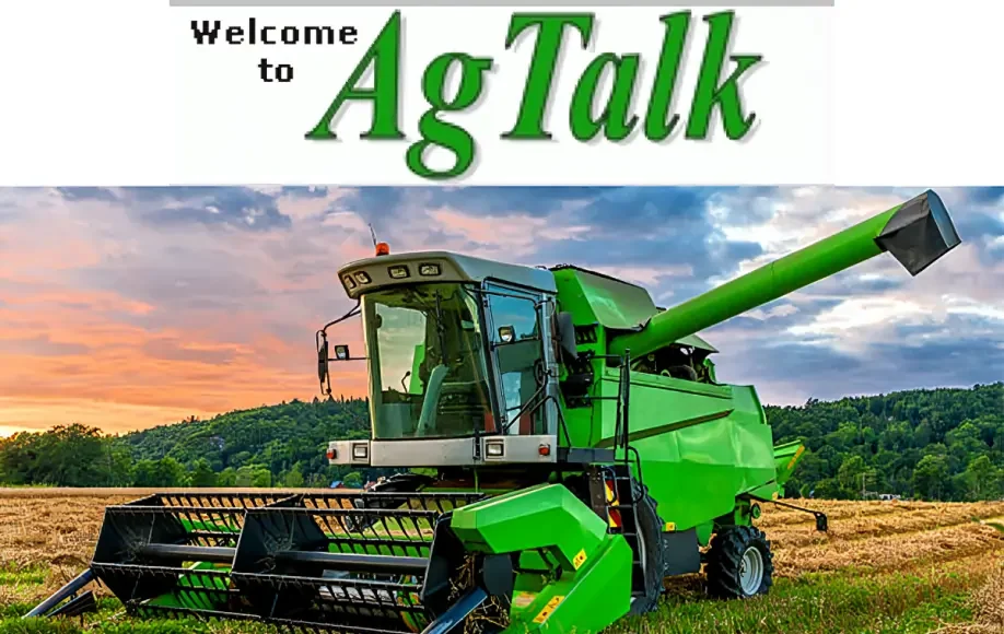 AgTalk image showing a green combine harvester in a harvested field at sunset with hills and trees in the background.