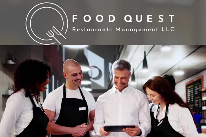 Food Quest Restaurants Management LLC team of chefs and manager smiling while looking at a tablet in a modern restaurant kitchen.