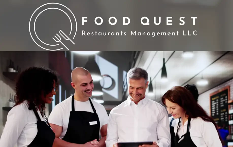 Food Quest Restaurants Management LLC team of chefs and manager smiling while looking at a tablet in a modern restaurant kitchen.