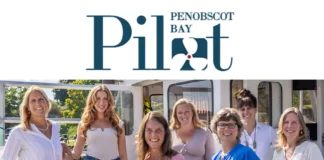 A group of smiling women stands in front of a boat under the Penobscot Bay Pilot logo, representing the PenBay Pilot team.