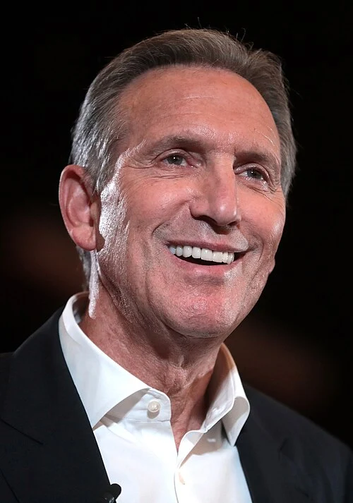 Former Starbucks CEO Howard Schultz smiling while speaking at an event.