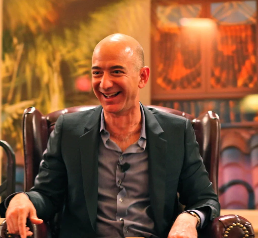 Amazon founder Jeff Bezos laughing while seated in a leather armchair during an event.