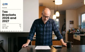 Tax Brackets 2026 and 2027: Federal Income Tax Rates and How They Work Man standing at a kitchen island with a calculator, reviewing his 2026 tax brackets on a printed sheet