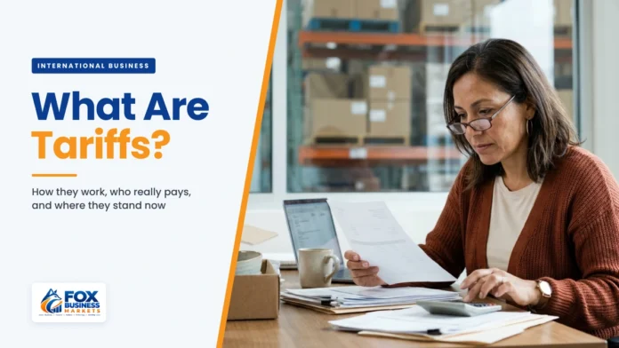What are tariffs explained: small business owner reviewing an import duty invoice with a calculator in her warehouse office